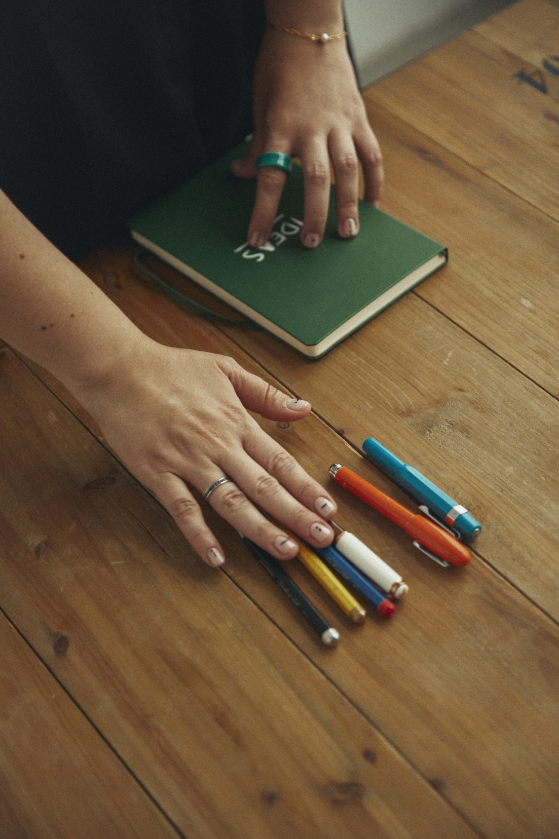 Manos de Susana Carrillo sobre una libreta verde y bolígrafos de colores, sobre una mesa de madera
